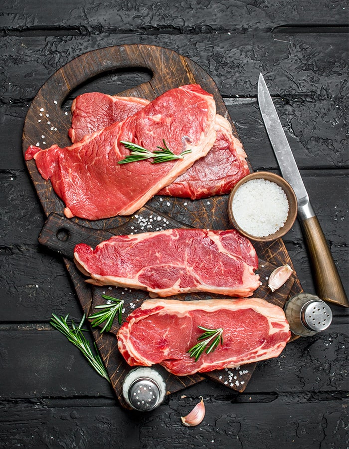Rohe Steaks mit Rosmarin und grobem Salz auf einem Holzbrett